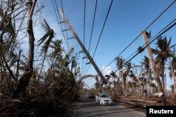 FILE PHOTO: Cars drive under a partially collapsed utility pole, after the island was hit by Hurricane Maria in September, in Naguabo, Puerto Rico, Oct. 20, 2017.