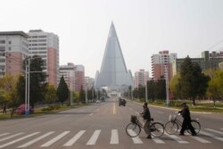 People wearing face masks cross a road in front of the Ryugyong Hotel in Pyongyang, North Korea Tuesday, April 28, 2020. (AP Photo/Cha Song Ho)
