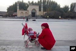In this Nov. 4, 2017, a woman tends to her child near the Id Kah Mosque in Kashgar in western China's Xinjiang region. (AP Photo/Ng Han Guan)
