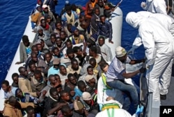 Migrants crowded in an inflatable dinghy await rescue by the Italian coast guard’s vessel Denaro off the Libyan coast, in the Mediterranean Sea, Wednesday, April 22, 2015. European Union leaders have promised more aid to help stem the tide of migrants and