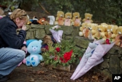 FILE - Cheryl Girardi, of Middletown, Conn., kneels beside 26 teddy bears, each representing a victim of the Sandy Hook Elementary School shooting, at a sidewalk memorial in Newtown, Conn., Dec. 16, 2012.