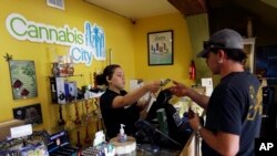 FILE - Jessica Mann, left, gives change to a customer following a recreational marijuana purchase at Cannabis City, in Seattle, July 7, 2016. Officials in states like Oregon where marijuana is legal are trying to curtail smuggling of pot to other states.