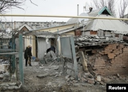 A woman cleans up debris near her house damaged by recent shelling in the rebel-held town of Yasynuvata, Ukraine, Dec. 21, 2017.