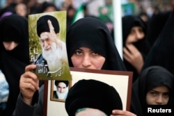 FILE - A woman holds pictures of Iran's Supreme Leader Ayatollah Ali Khamenei (top) and late Leader Ayatollah Ruhollah Khomeini during a rally to mark the 32nd anniversary of the Islamic Revolution in Qom.