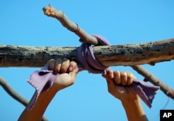 A migrant uses cloth to tie tree branches while building a rain cover for his tent in a makeshift camp in Horgos, Serbia, Sept. 30, 2016.