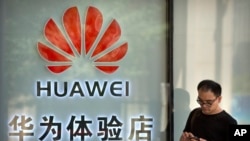 FILE - A man uses his smartphone outside of a shop selling Huawei products at a shopping mall in Beijing, May 29, 2019. 