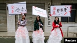 FILE - University students dressed as battered wives hold banners in front of an office of China's Civil Affairs department, where local people register for marriage, in protest of domestic violence, during the International Day for the Elimination of Vio