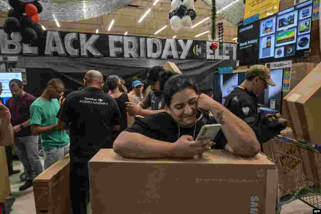 A woman watches her phone while shoppers buy TV sets at a supermarket during a Black Friday sale in Sao Paulo on November 28, 2024.