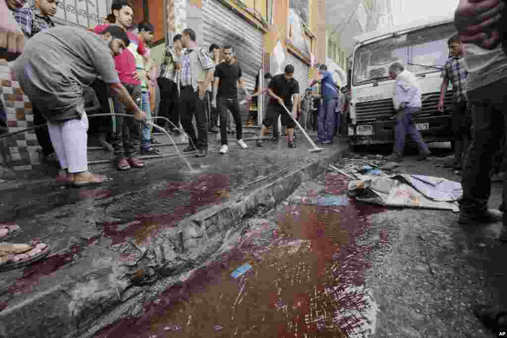 Palestinians wash blood from a sidewalk where seven Palestinians where killed in an Israeli air strike in Gaza City, July 12, 2014. 