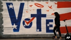 រូបឯកសារ៖ ស្ត្រី​ម្នាក់ ដើរ​ឆ្លងកាត់​ជញ្ជាំង​ដែល​មាន​សំណេរ​ថា «បោះឆ្នោត» កាលពី​ថ្ងៃទី២ ខែវិច្ឆិកា ឆ្នាំ២០២០ នៅ​ទីក្រុង Los Angeles រដ្ឋ California។