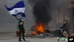 A masked protester waves a Nicaraguan national flag in front of a burning barricade, as protesters clashed with riot police in the Monimbo district of Masaya, Nicaragua, May 12, 2018.