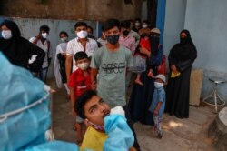 A health worker takes a nasal swab sample of a man to test for COVID-19 as others wait their turn to get tested at a hospital in Hyderabad, India, April 19, 2021.