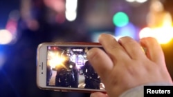 FILE - A demonstrator records law enforcement officers at a protest against police violence and racial inequality during unrest in Portland, Oregon, Sept. 27, 2020. 