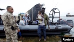 Un migrant portant un enfant, débarque d’un bateau de l’armée sous la surveillance d’un militaire de la marine libyenne à Tripoli, Libye, 7 septembre 2015