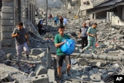 Warga Palestina berjalan melewati puing-puing bangunan yang hancur akibat serangan udara Israel di Kota Gaza pada Selasa, 10 Oktober 2023. (Foto: AP)