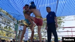 Nanthawat Pomsod (tengah), 11 tahun, seorang petinju anak, berlaga melawan Kritthonglek Sitkritthongkam (kiri), dalam pertandingan tinju di sebuah kuil, di Provinsi Buriram, Thailand, 2 Februari 2018. 