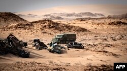 Un véhicule de l'armée marocaine passe devant des épaves de voitures à Guerguerat situé au Sahara occidental, le 24 novembre 2020, après l'intervention des forces armées royales marocaines dans la région.