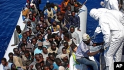 Migrants crowded in an inflatable dinghy await rescue by the Italian coast guard’s vessel Denaro off the Libyan coast, in the Mediterranean Sea, Wednesday, April 22, 2015. European Union leaders have promised more aid to help stem the tide of migrants and