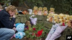 FILE - Cheryl Girardi, of Middletown, Conn., kneels beside 26 teddy bears, each representing a victim of the Sandy Hook Elementary School shooting, at a sidewalk memorial, Dec. 16, 2012, in Newtown, Conn.