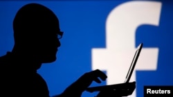 FILE - A man is silhouetted against a video screen with an Facebook logo in this photo illustration, Aug. 14, 2013. 