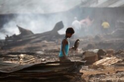 FILE - A boy searches for useful items among the ashes of burned dwellings after a fire destroyed shelters at a camp for internally displaced Rohingya Muslims in Myanmar's western Rakhine state near Sittwe, May 3, 2016.