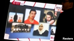 Seorang pria di Tokyo berjalan melewati layar televisi yang menayangkan berita mengenai pertukaran sandera dengan tahanan Yordania.