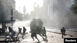 Para pengunjuk rasa anti-pemerintah melarikan diri untuk menghindari semburan meriam air dari polisi anti-huru-hara di Santiago, Chile, 29 Oktober 2019.