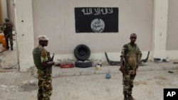 Des soldats nigérians se tiennent à un poste de contrôle devant un drapeau de Boko Haram la ville de Damasak, Nigeria, 18 mars 2015.