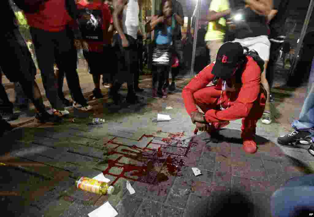 A man squats near a pool of blood after a man was injured during a protest of Tuesday's fatal police shooting of Keith Lamont Scott in Charlotte, N.C., Sept. 21, 2016. 