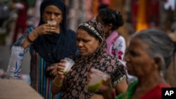 Shoppers drink juice in plastic glasses as they take a break at a weekly market in New Delhi, India, Wednesday on June 29, 2022. (AP Photo/Altaf Qadri)