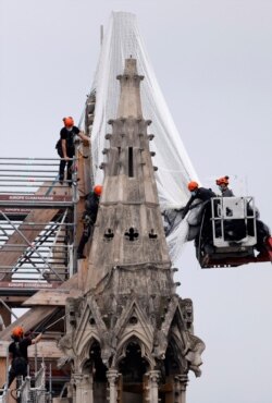 Workers prepare to remove damaged scaffolding elements from the remains of the damaged roof of Notre Dame Cathedral in Paris, June 8, 2020