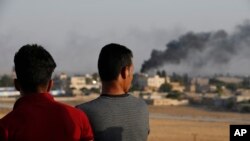 People standing on a rooftop in Akcakale, Sanliurfa province, southeastern Turkey, at the border with Syria, watch as in the background smoke billows from fires caused by Turkish bombardment in Tal Abyad, Syria, Sunday, Oct. 13, 2019.