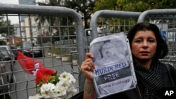 Sahar Zeki, an activist and a friend of slain Saudi writer Jamal Khashoggi, holds a picture of him, after attaching a bouquet of flowers, at the barriers blocking the road leading to the Saudi Arabia's consulate in Istanbul, Tuesday, Oct. 23, 2018. Saudi officials murdered journalist Jamal Khashoggi in their Istanbul consulate after plotting his death for days, Turkey's president said Tuesday, contradicting Saudi Arabia's explanation that the writer was accidentally killed. He demanded that the kingdom reveal the identities of all involved, regardless of rank.