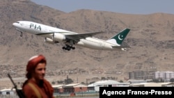 FILE - A Taliban fighter stands guard as a Pakistan International Airlines plane, the first commercial international flight to land since the Taliban retook power, takes off at the airport in Kabul on Sept. 13, 2021.