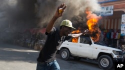 A protester runs past a burning car during a protest against President Michel Martelly's government in Port-au-Prince, Haiti, Jan. 18, 2016.