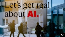 People reflected in a window of a hotel at the Davos Promenade with a slogan about AI alongside the World Economic Forum in Davos, Switzerland, Monday, Jan. 15, 2024. (AP Photo/Markus Schreiber)