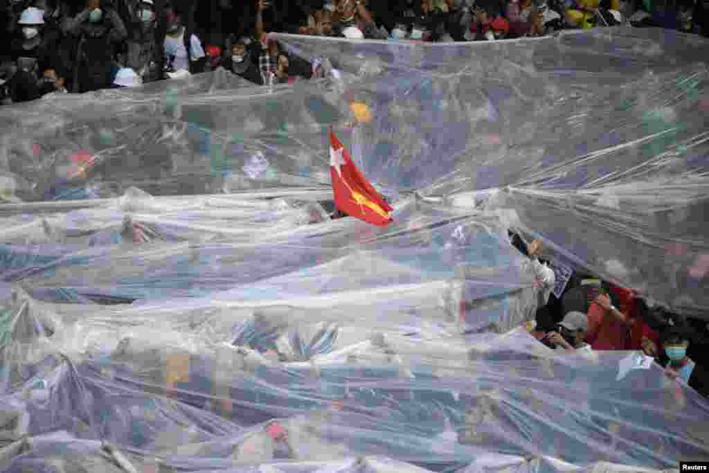People cover under plastic sheets to protect themselves from a water canon during a rally against the military coup and to demand the release of elected leader Aung San Suu Kyi, in Yangon, Myanmar.