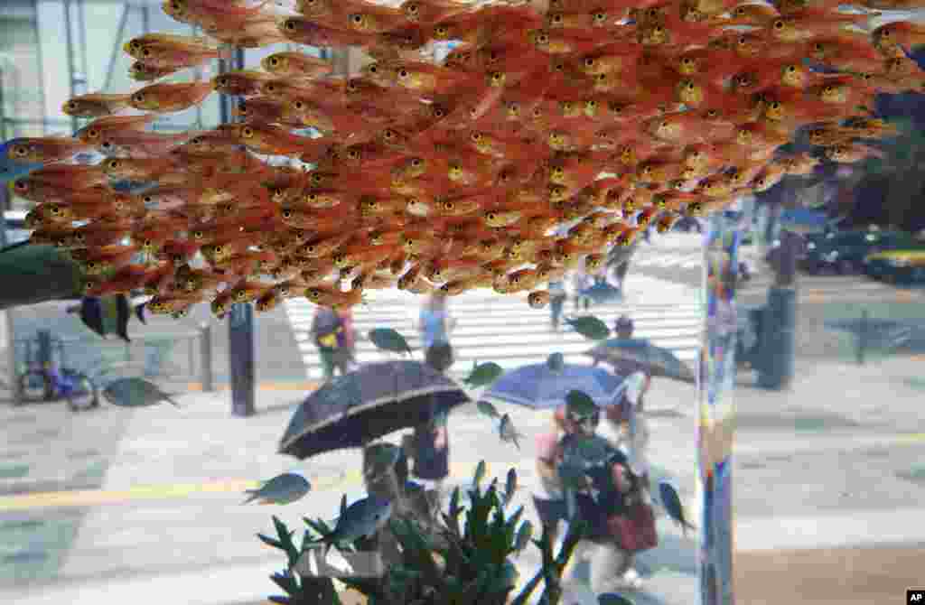 Passers-by look at fish swimming in a large glass tank displayed at Ginza shopping district in Tokyo, Japan.
