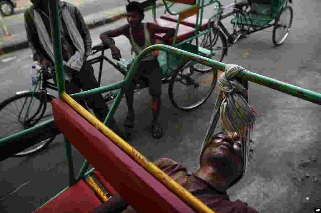 Seorang tukang becak di India menggunakan syal untuk mengikat kepalanya saat beristirahat di sebuah pinggir jalan di New Delhi.