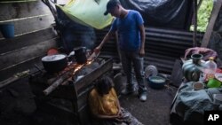 Pascuala Jonaj sits against a wood-burning stove as her son Victor Cal feeds the fire a day before he begins his trip to the United States, inside their home at the makeshift settlement Nuevo Queja, Guatemala, Thurs., July 8, 2021. (AP Photo/Rodrigo Abd)