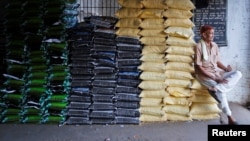 FILE - A laborer sits on sacks of food grains while waiting for customers at a wholesale market in Ahmedabad, India, Dec. 14, 2016. 
