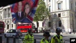 Police walk past a flag hanging outside a coffee shop, depicting Britain's Prince William and Kate Middleton, in Whitehall, in central London, April 27, 2011
