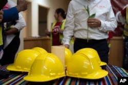 Construction workers and supporters gather around six construction helmets and a candle at a March 29, 2024, vigil by CASA of Maryland, a community advocacy group, to remember the six workers killed in the collapse of the Francis Scott Key Bridge in Baltimore.