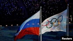 FILE - The Russian national flag flutters next to the Olympics flag during the closing ceremony for the 2014 Sochi Winter Olympics, Feb. 23, 2014.
