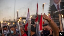 Anti-government protesters hold torches as they light a flame over a metal statue that reads in Arabic "October 17, Revolution," next to the site of the Aug. 4 blast in the seaport of Beirut that killed scores, in Beirut, Lebanon, Oct. 17, 2020.