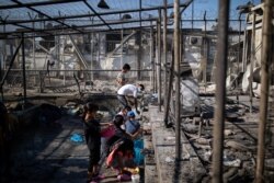 Refugees and migrants gather water next to destroyed shelters following a fire at the Moria camp on the island of Lesbos, Greece, Sept. 9, 2020.