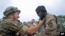 US and Ukrainian servicemen talk during the opening ceremony for the Rapid Trident/Saber Guardian 2015 military exercises at the International Peacekeeping and Security Center base outside Lviv, Ukraine, July 20, 2015.