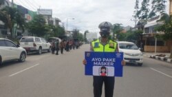 Seorang anggota Polisi membawa pesan sosialisasi agar memakai masker saat berlangsungnya operasi Yustisi yang digelar di Kota Palu, Kamis (24/09/2020) (Foto: VOA/Yoanes Litha)