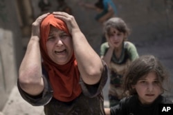 FILE - A woman screams while fleeing with her family through a destroyed alley, as Iraqi Special Forces continue their advance against Islamic State group militants, in the Old City of Mosul, Iraq, July 2, 2017.