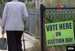 ស្ត្រីវ័យជរាម្នាក់​ដើរកាត់​ផ្លាក​សញ្ញាបោះឆ្នោតដែល​ភ្ជួរជាប់នឹង​របង​សាលារៀន​មួយ​នៅ​ទីក្រុងឡូវែល កាលពី​ថ្ងៃព្រហស្បតិ៍ ទី៨ ខែកញ្ញា ឆ្នាំ២០១៦។